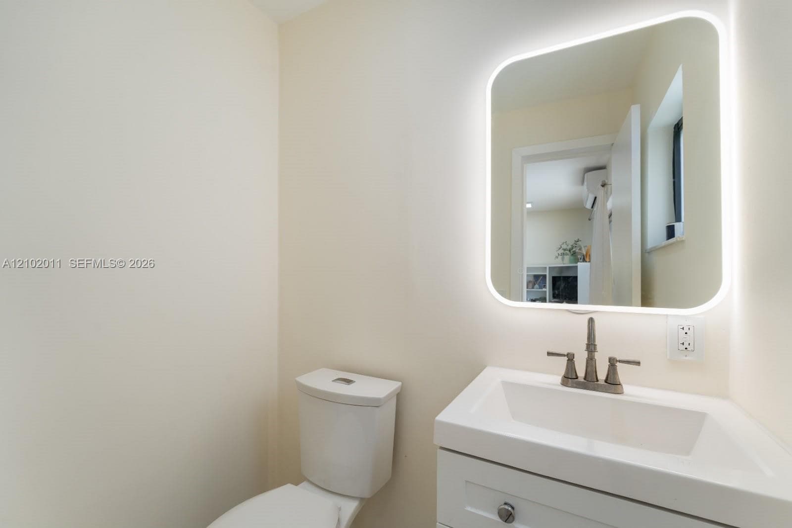 Illuminated mirror over a white vanity with an integrated sink and a two-handle faucet
