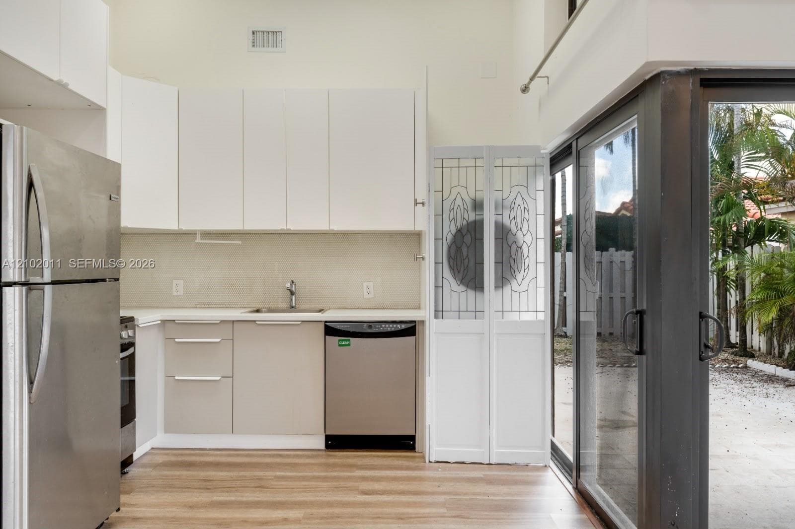 Kitchen featuring wood-finish flooring, stainless steel appliances, white cabinetry, and a sliding glass door to an outdoor area