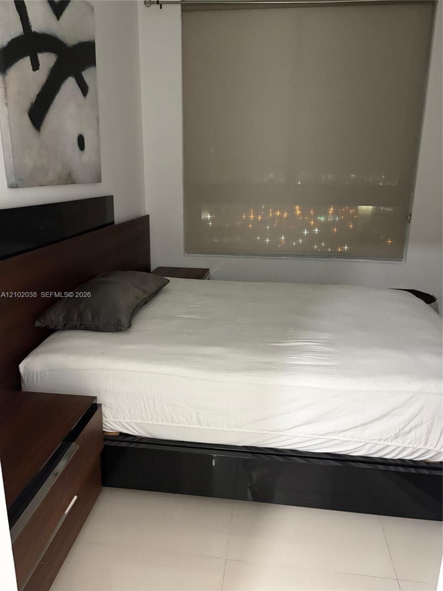 Built-in wood-finish headboard with integrated cabinetry, large-format tile flooring, and a floor-to-ceiling roller shade