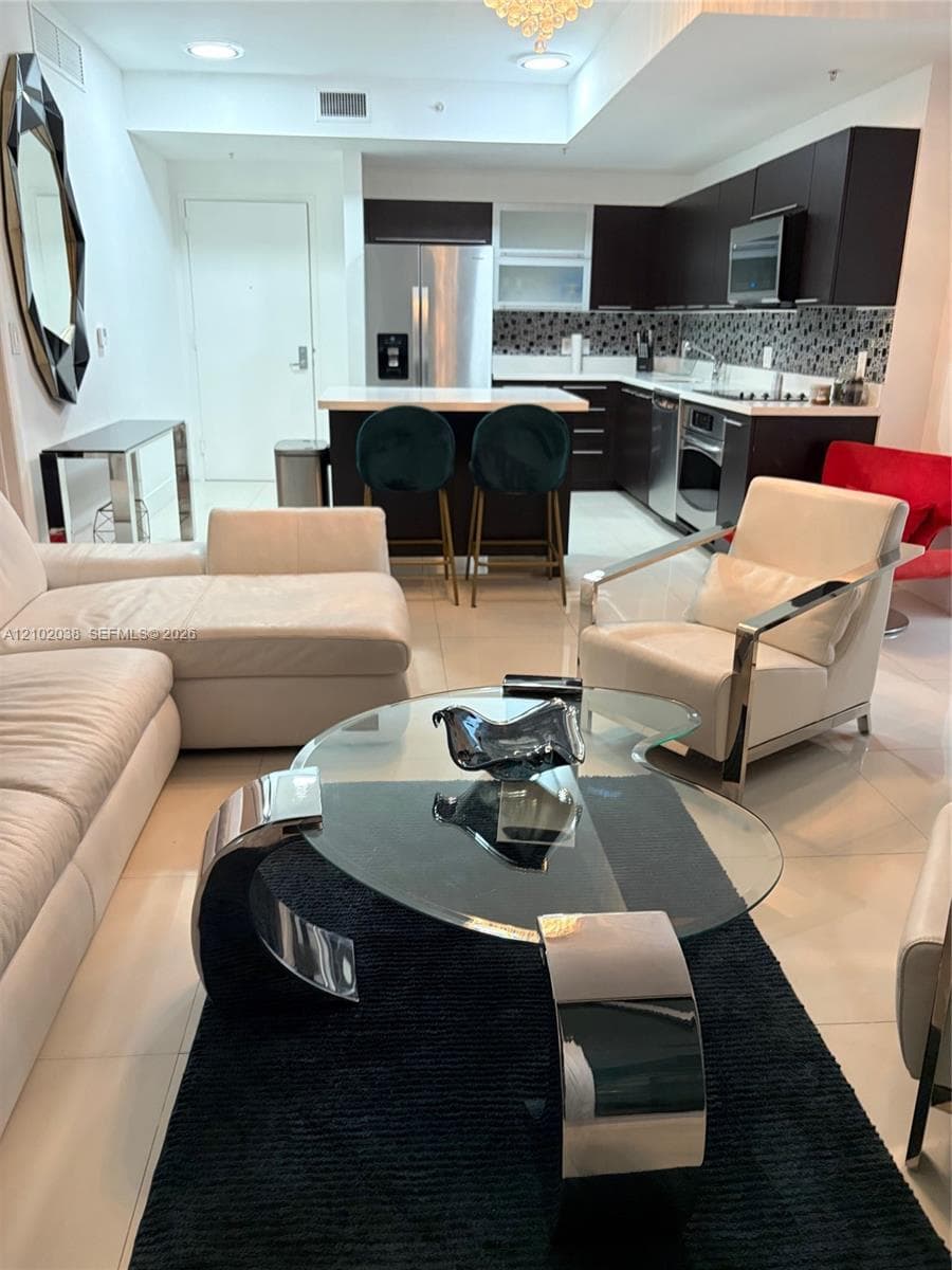 Kitchen featuring dark wood-finish cabinetry, stainless steel appliances, a stone countertop, and a tiled backsplash, complemented by large-format porcelain flooring