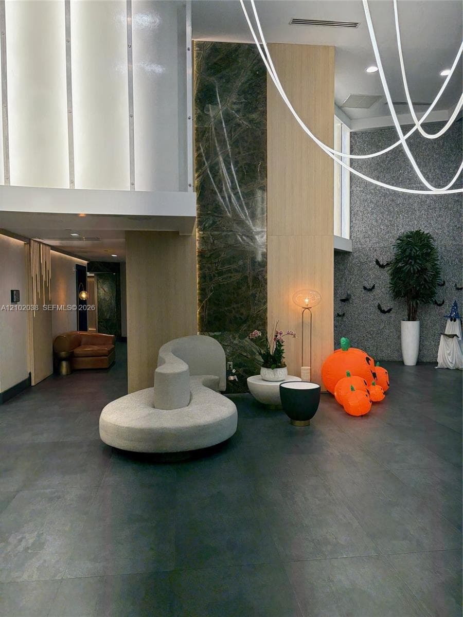 Lobby featuring high ceilings with integrated LED lighting, stone wall accents, large-format tile flooring, and custom wood paneling