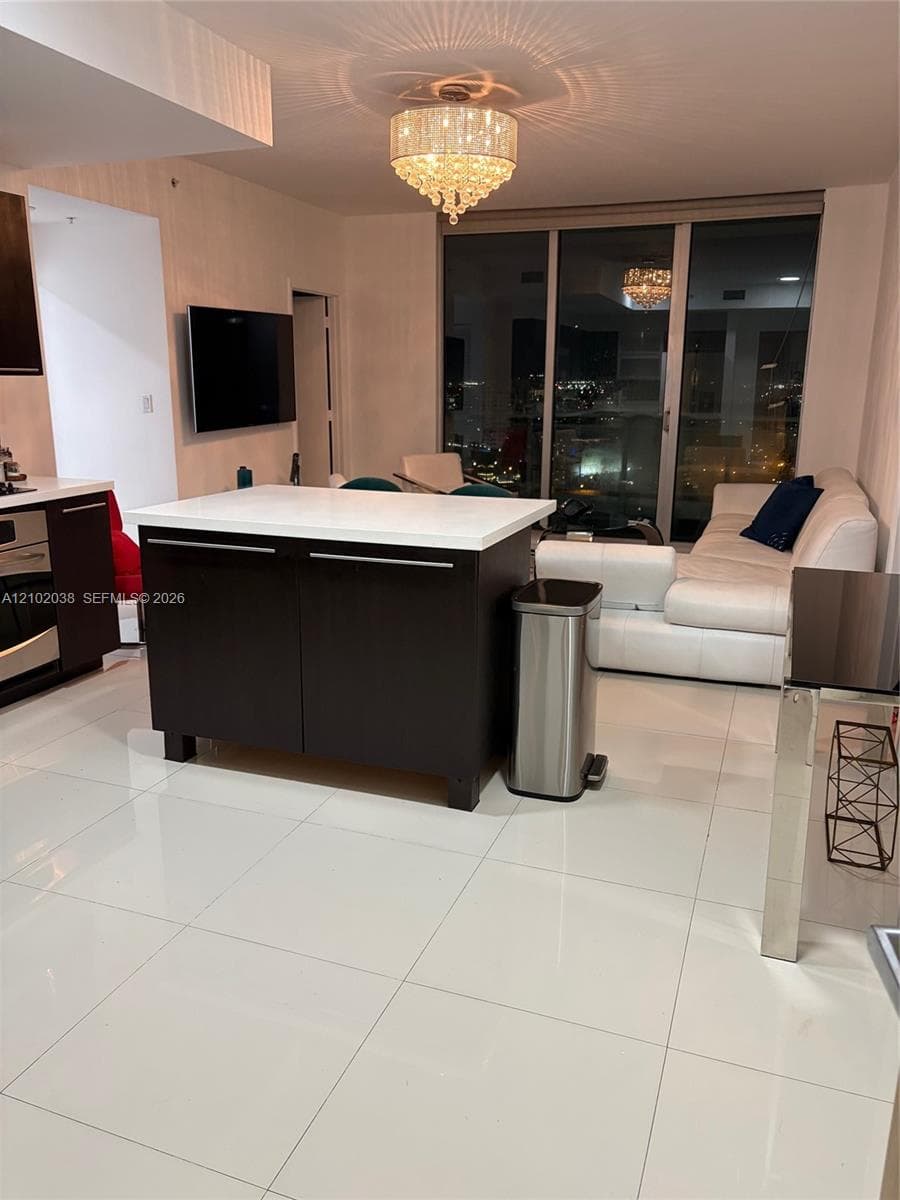 Kitchen island with stone-finish countertop, polished tile flooring, crystal chandelier lighting, and floor-to-ceiling glass windows