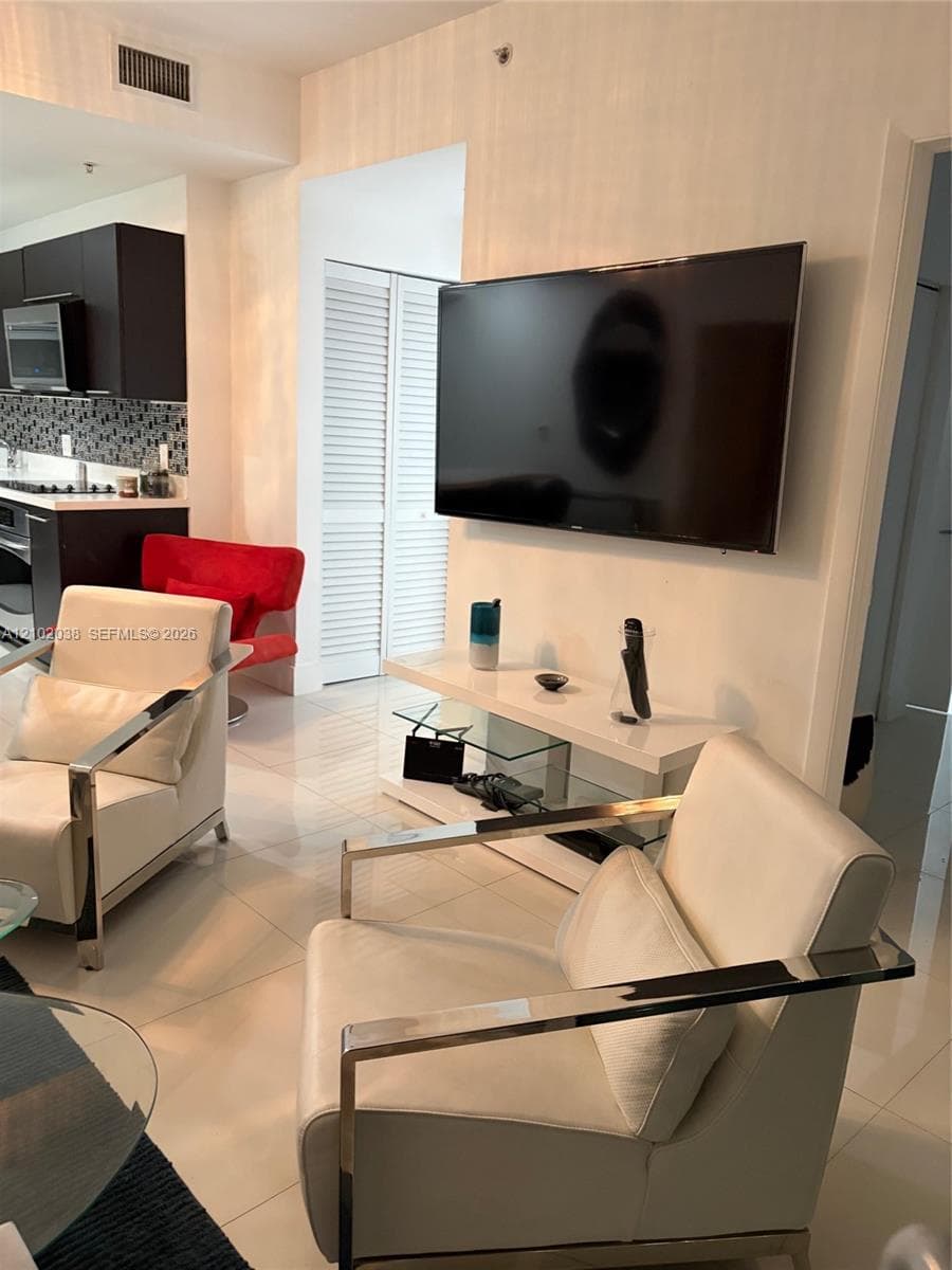 Polished porcelain tile flooring, dark-toned cabinetry, mosaic-tile backsplash, and louvered closet doors