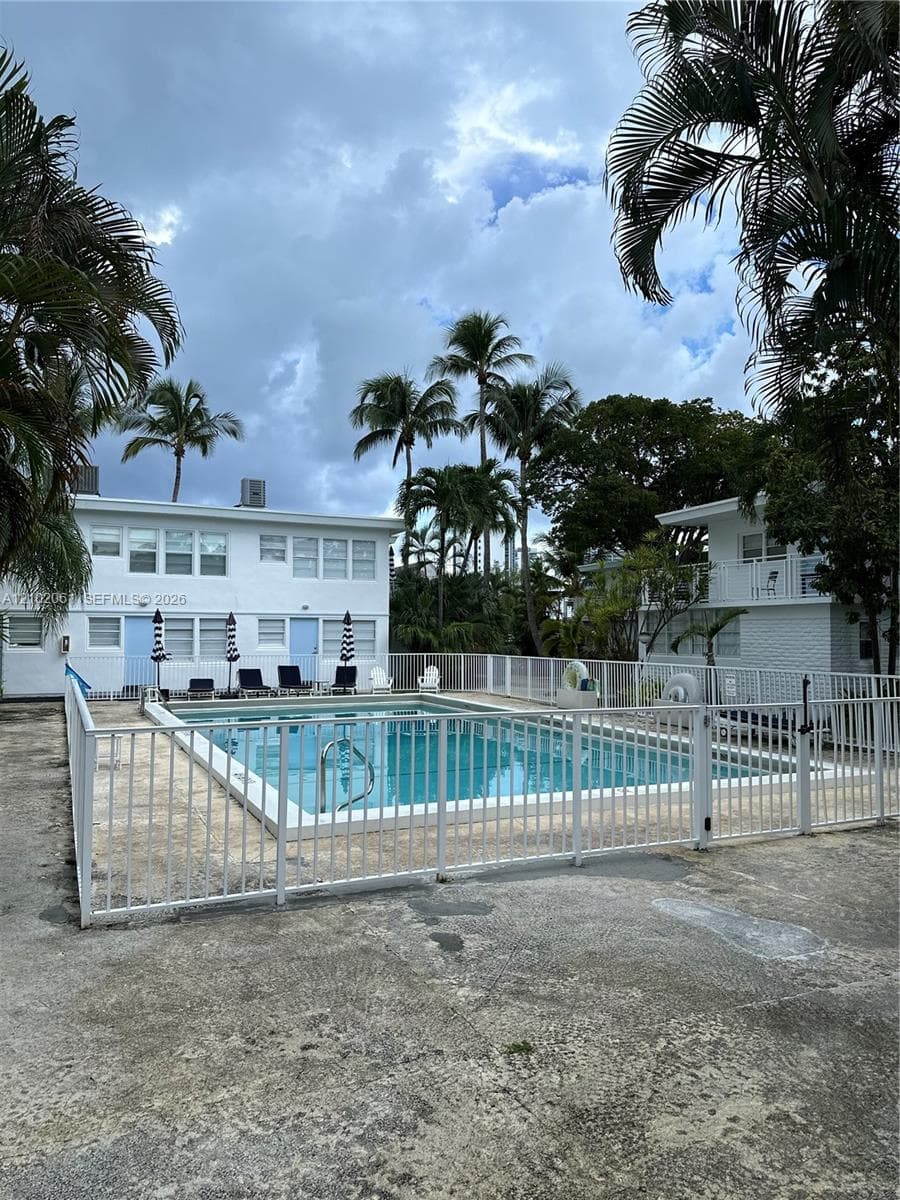 Outdoor pool area featuring a white perimeter fence, integrated pool steps, and surrounding concrete paving
