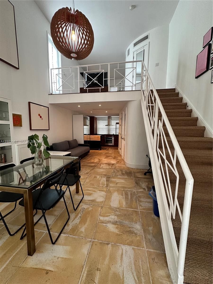 Loft-style living space featuring high ceilings, a mezzanine level with white geometric railings, a built-in kitchen, and a carpeted staircase