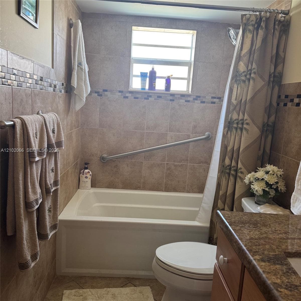 Full-height wall tiling with decorative mosaic inlay, deep soaking tub with integrated stainless steel grab bar, and stone-finish vanity countertop