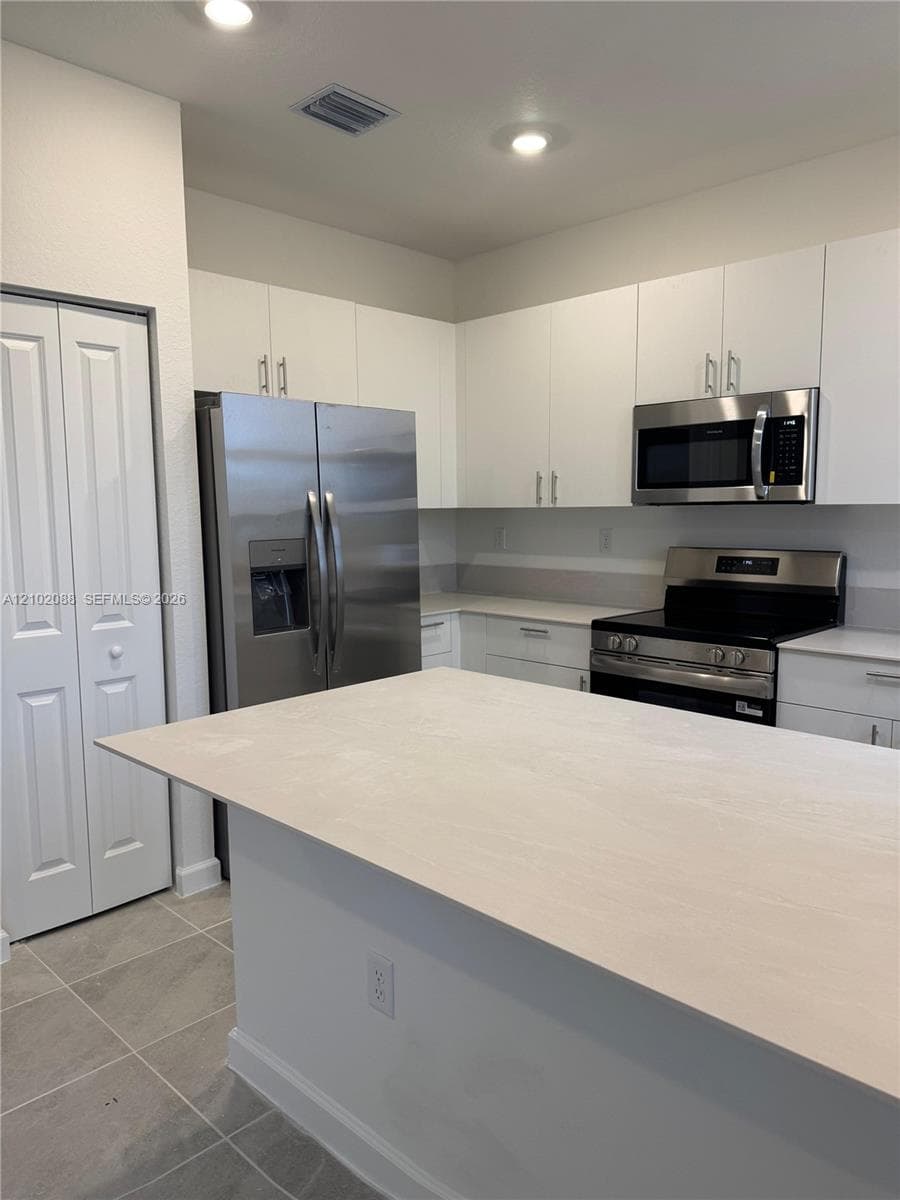 Kitchen featuring white flat-panel cabinetry, a central island with a countertop, stainless steel appliances, and tile flooring