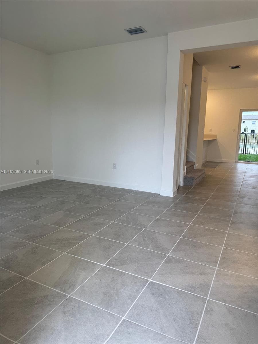 Large-format neutral tile flooring throughout, high ceilings, and a glass-paneled exterior door