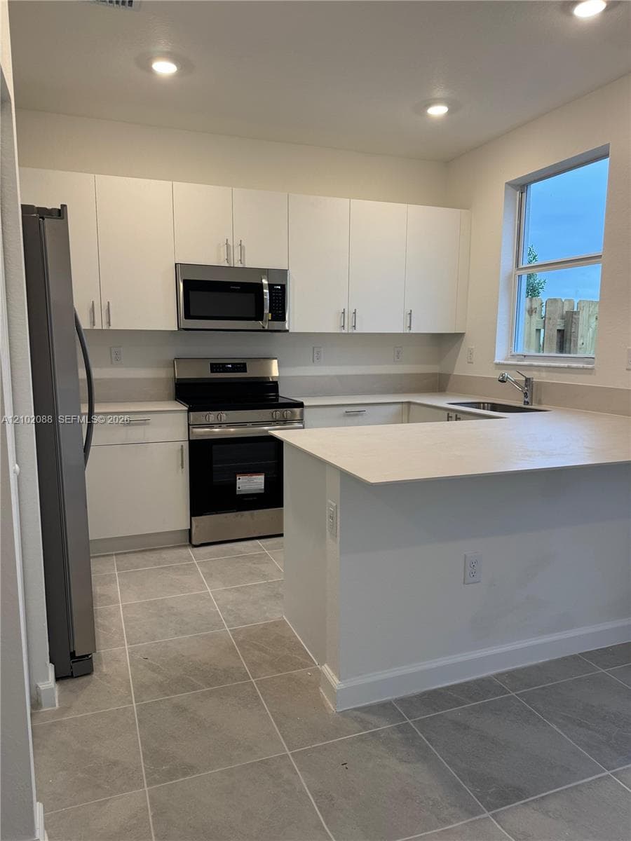 Kitchen featuring white cabinetry, stainless steel appliances, neutral solid-surface countertops, tile flooring, and recessed lighting