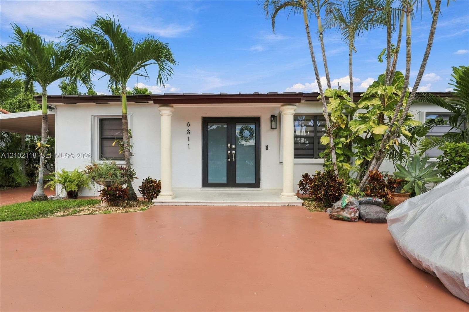 Single-story exterior featuring a covered entryway with dual fluted columns, double glass-panel front doors, smooth stucco siding, and a paved driveway