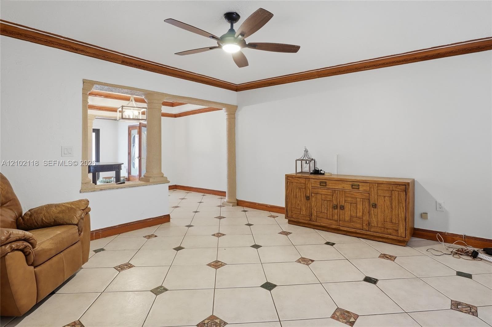 Interior space featuring tile flooring with decorative inserts, crown molding, a decorative columned pass-through opening, and a ceiling fan with integrated lighting
