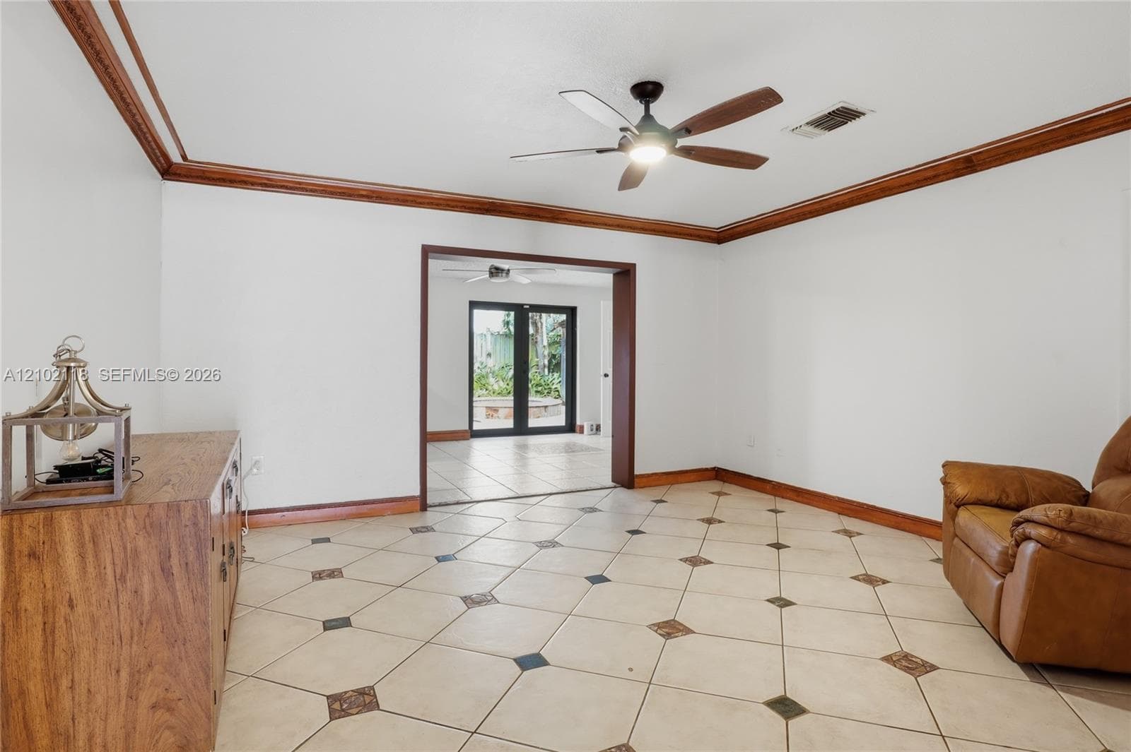 Interior space featuring diagonal tile flooring with decorative stone insets, extensive wood crown molding, and a multi-blade ceiling fan
