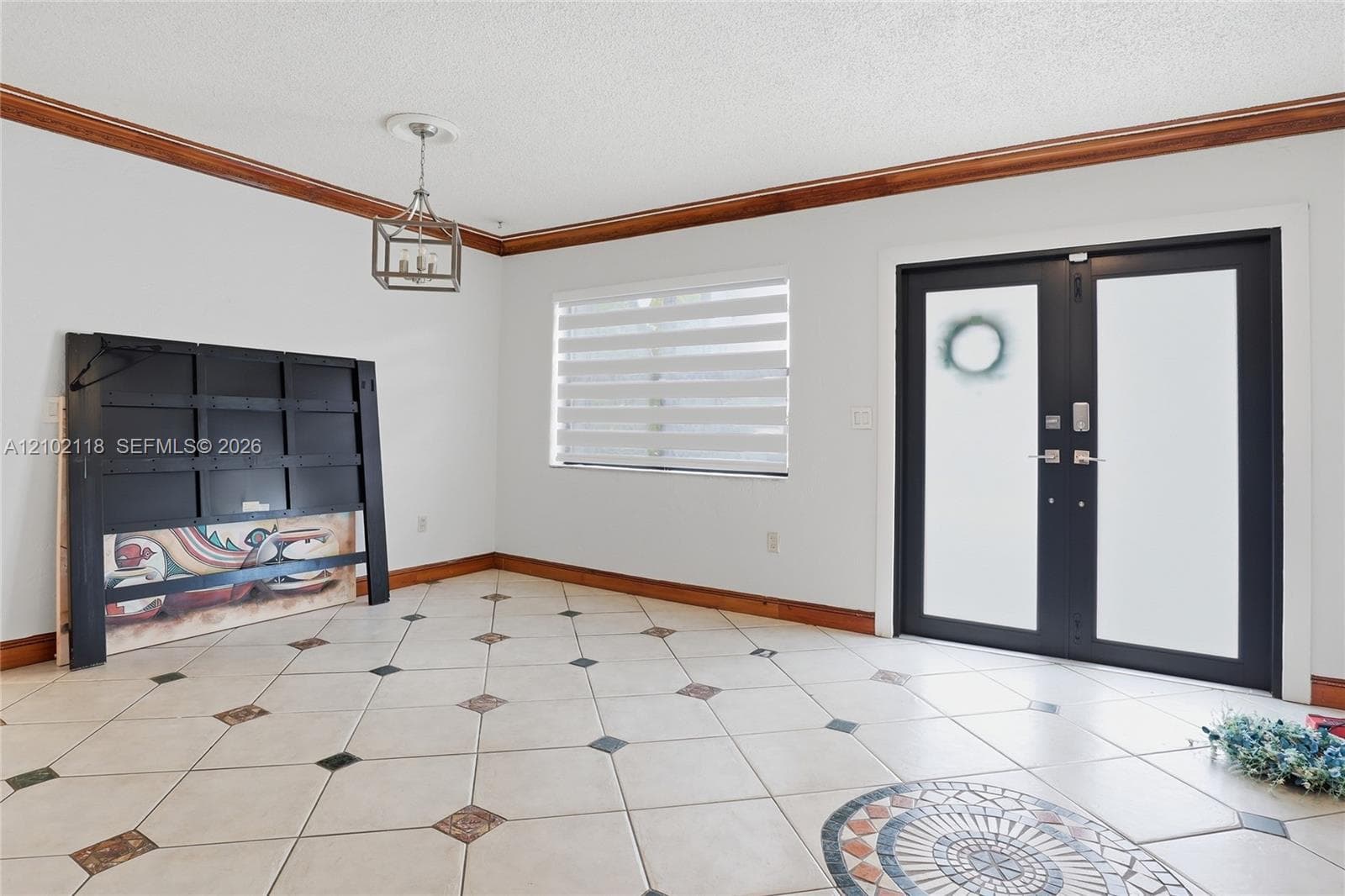 Double entry doors with frosted glass panels, ceramic tile flooring with decorative inlay, crown molding, and a tiered metal chandelier