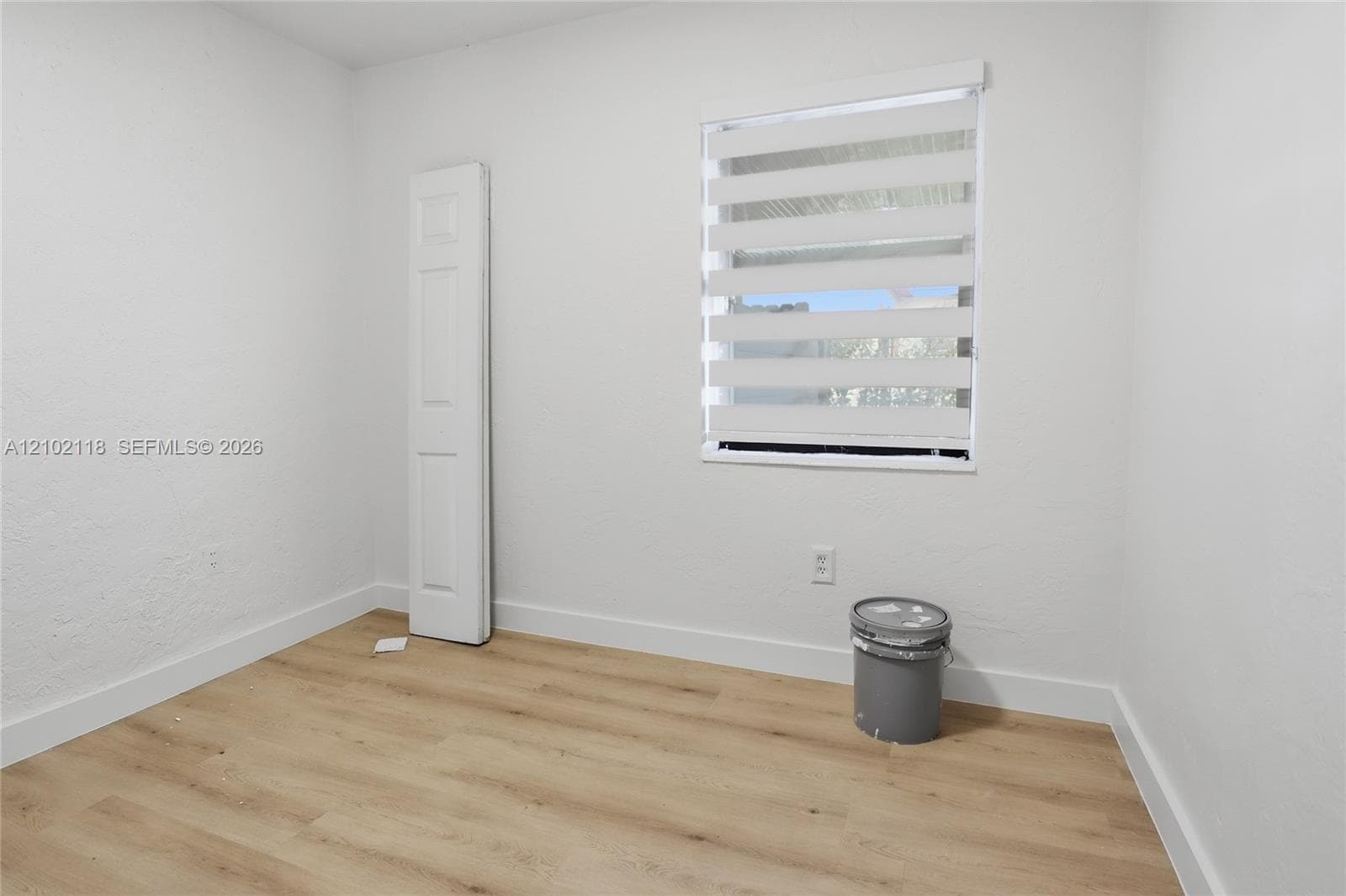 Interior room featuring wood-finish flooring, crisp white wall finishes, a single-panel interior door, and a horizontal banded window treatment