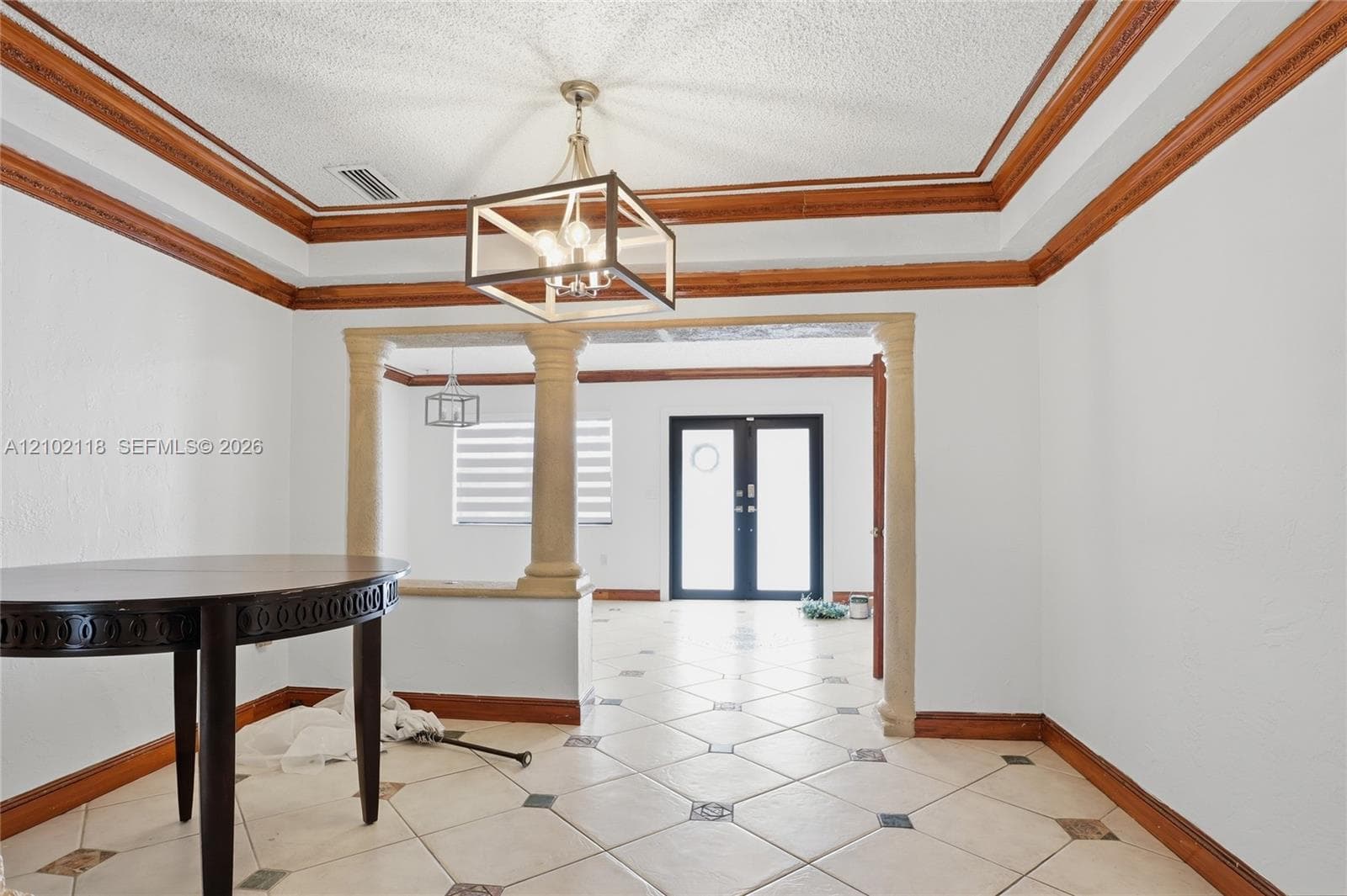 Tray ceiling with wood trim, decorative stone columns, geometric pendant lighting, and ceramic tile flooring with inlay detailing