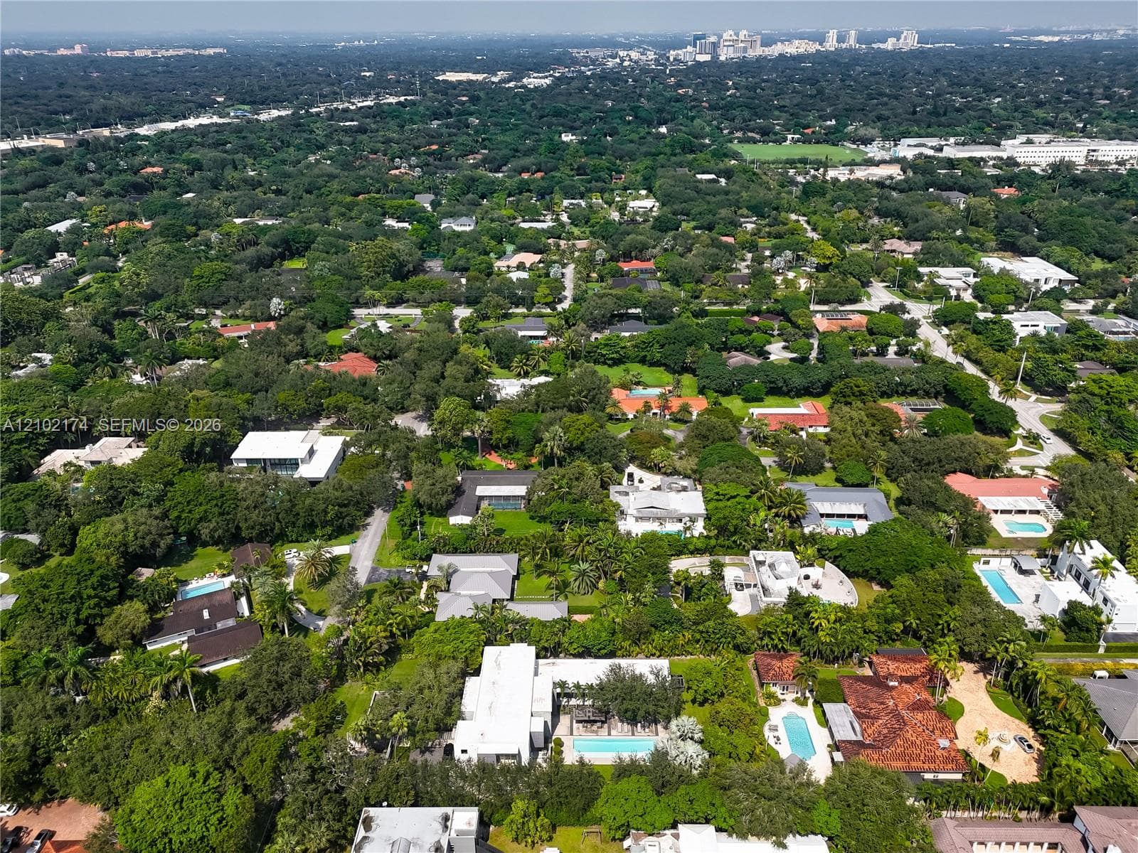 Aerial perspective of a property featuring an in-ground swimming pool, mature perimeter landscaping, and extensive tree cover within a dense residential setting