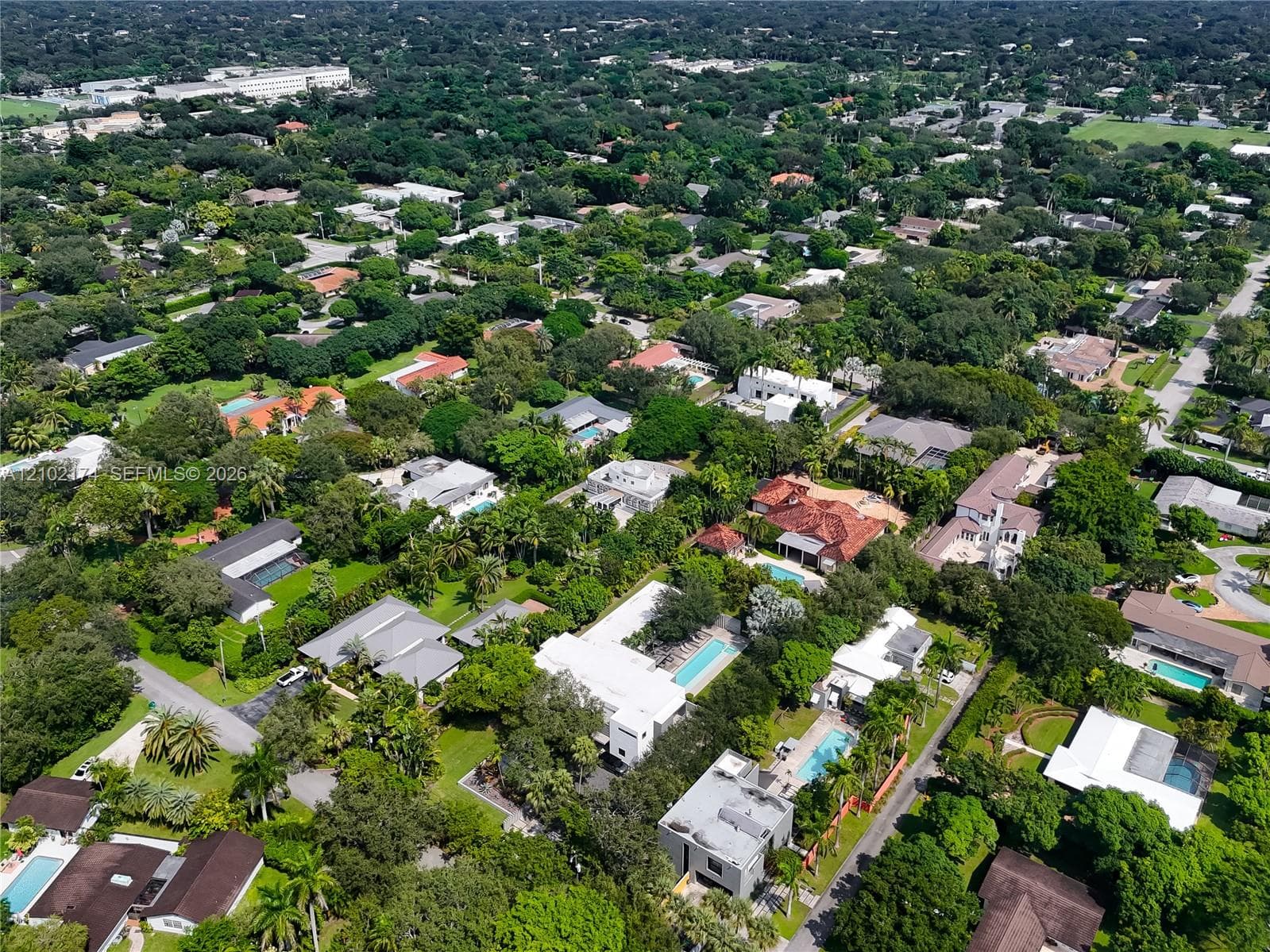 Aerial perspective of a multi-level contemporary estate featuring a rectangular swimming pool, integrated hardscaping, established perimeter landscaping, and mature foliage