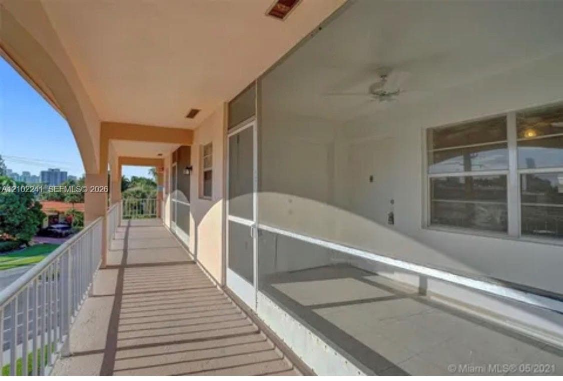 Covered exterior balcony featuring a metal railing, screened-in enclosure, and ceiling fan