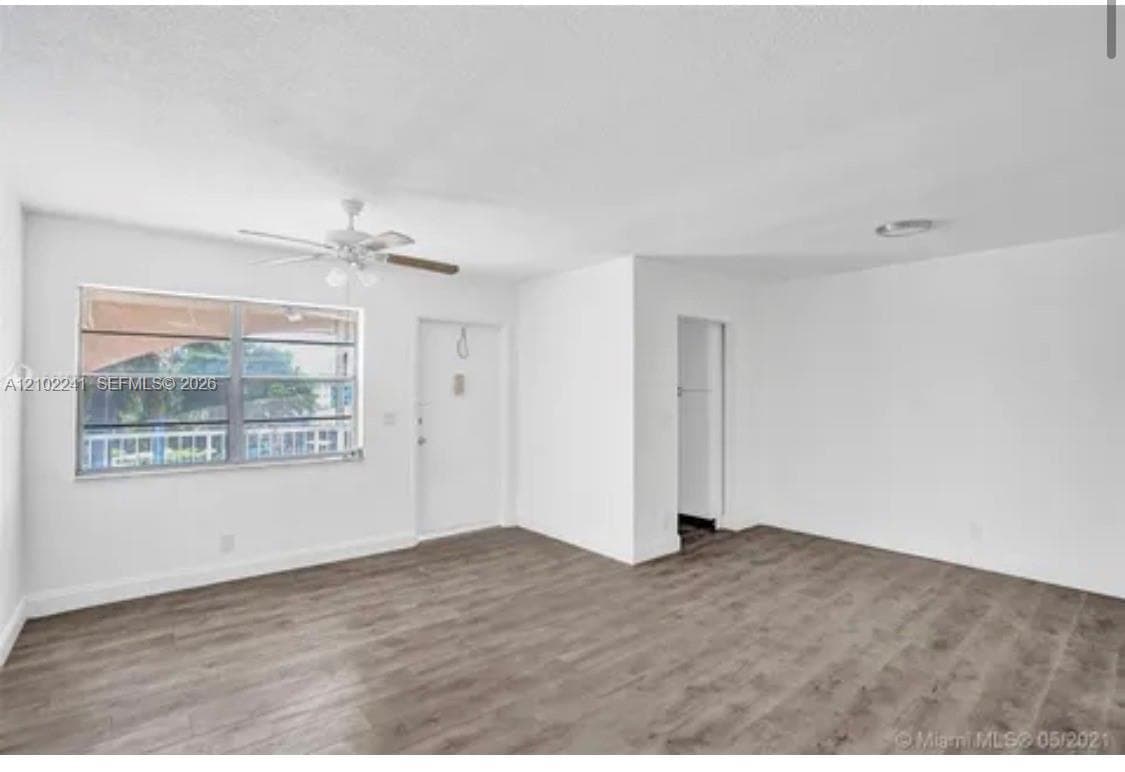 Neutral interior featuring wood-finish flooring, a multi-pane horizontal sliding window, a white single-panel entry door, and a ceiling-mounted fan with integrated light fixture