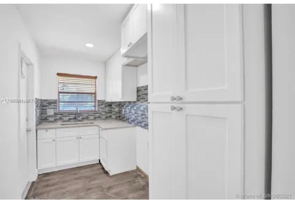 Kitchen featuring white shaker-style cabinetry, a floor-to-ceiling pantry, stone-patterned tile backsplash, neutral countertops, and wood-finish flooring