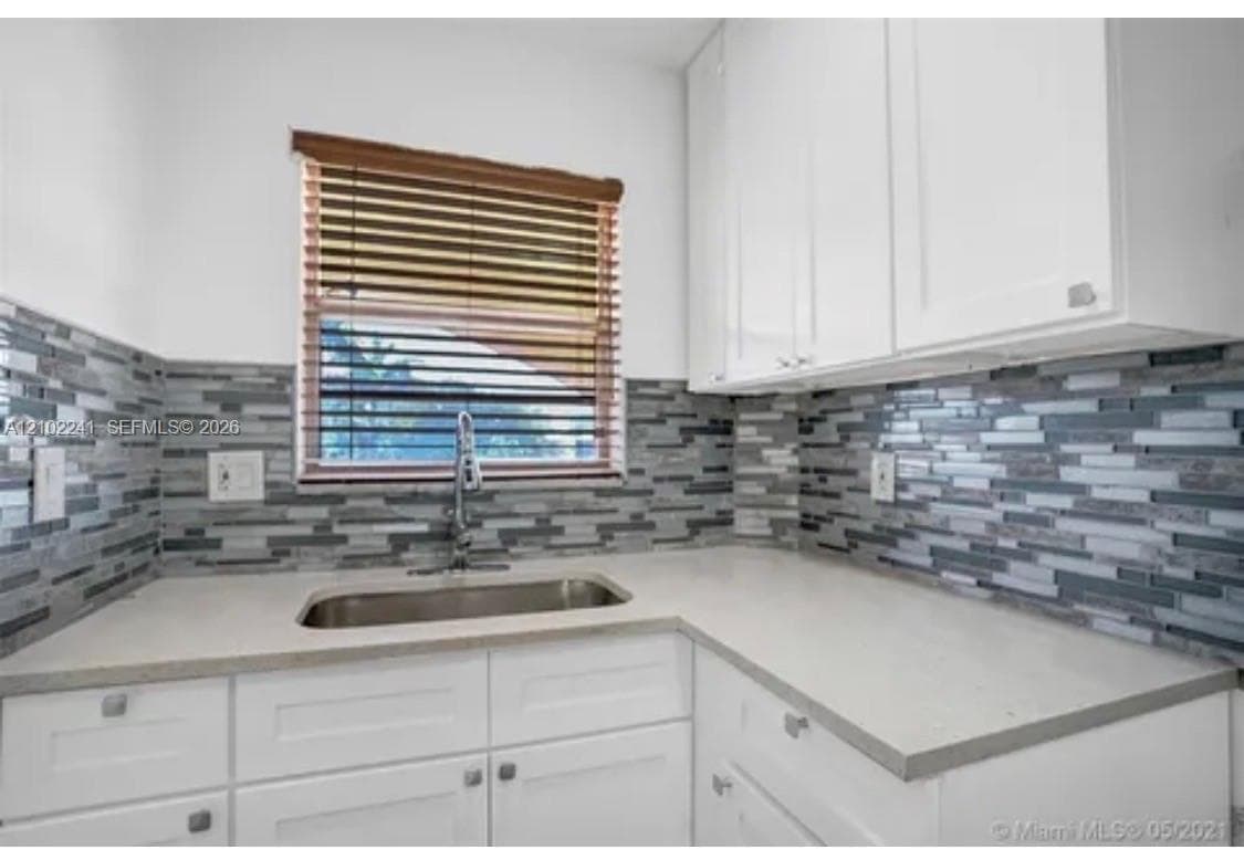 Kitchen featuring white shaker-style cabinetry, quartz countertops, a multi-tonal linear tile backsplash, and an undermount stainless steel sink with a high-arc faucet