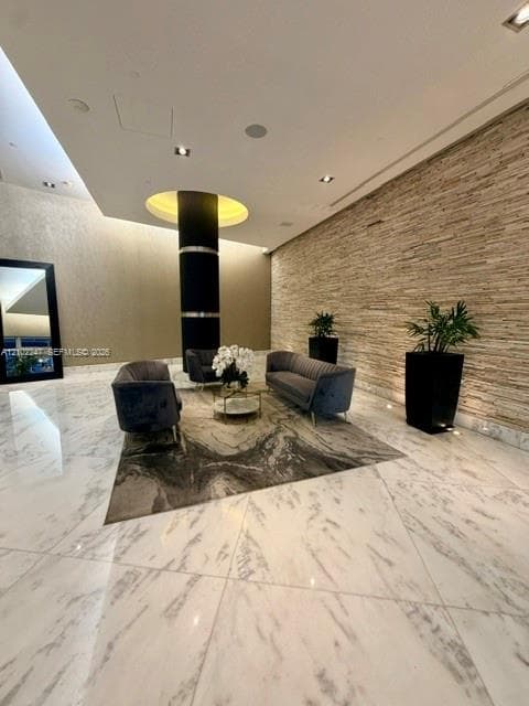Lobby featuring polished stone flooring, a floor-to-ceiling textured stone accent wall, recessed ceiling lighting, and a cylindrical support column with a circular recessed cove