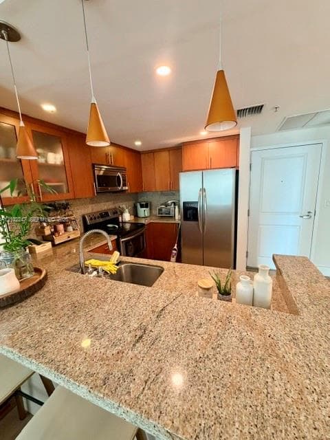 Kitchen featuring stone countertops, natural wood cabinetry, stainless steel appliances, and pendant lighting