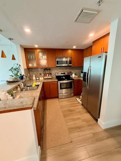 Kitchen featuring wood cabinetry, stone countertops, stainless steel appliances, and wood-finish flooring