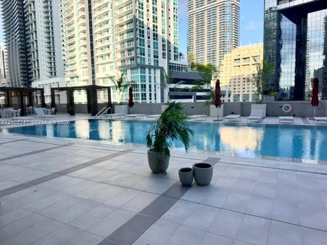 Outdoor swimming pool featuring a tiled deck, decorative pergola structure, and built-in metal handrails