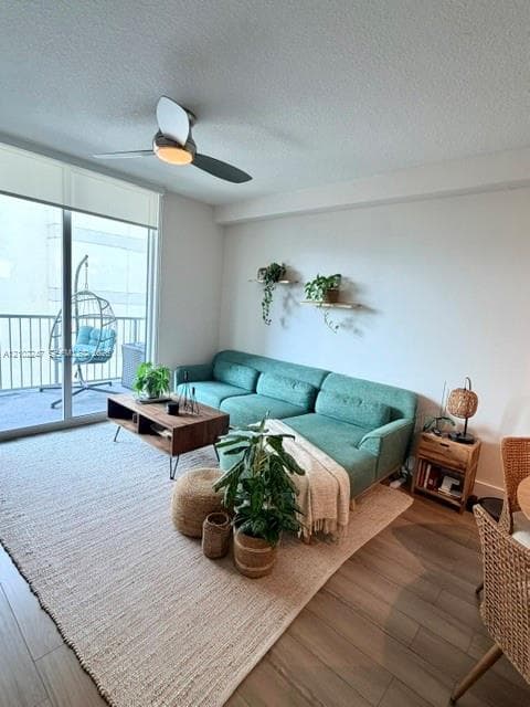 Living area featuring wood-finish flooring, a contemporary three-blade ceiling fan with integrated lighting and sliding glass doors with direct access to a private balcony