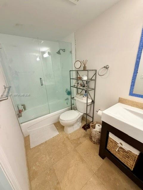 Full bathroom featuring stone-tiled flooring, a tub-shower combination with a glass enclosure, and a dark-toned vanity with a white integrated sink