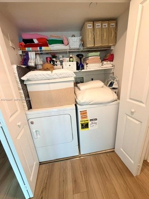 Laundry closet featuring white side-by-side appliances, multi-level shelving, and wood-finish flooring