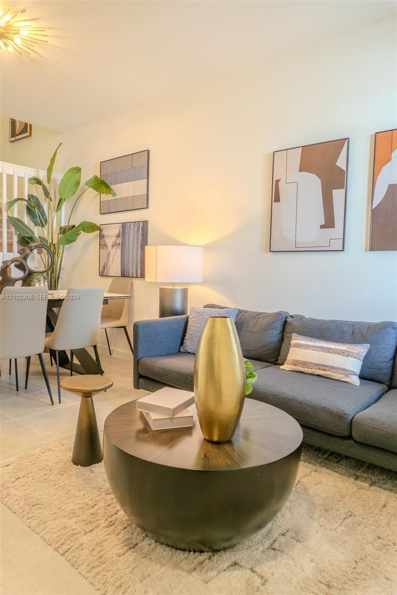 Open-concept space featuring neutral tile flooring, sunburst-style ceiling light fixture, and crisp white wall finishes