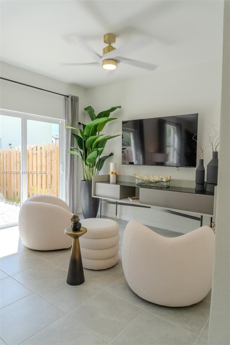 Large-format neutral floor tile, gold-finish ceiling fan with integrated lighting, and glass sliding door providing exterior access