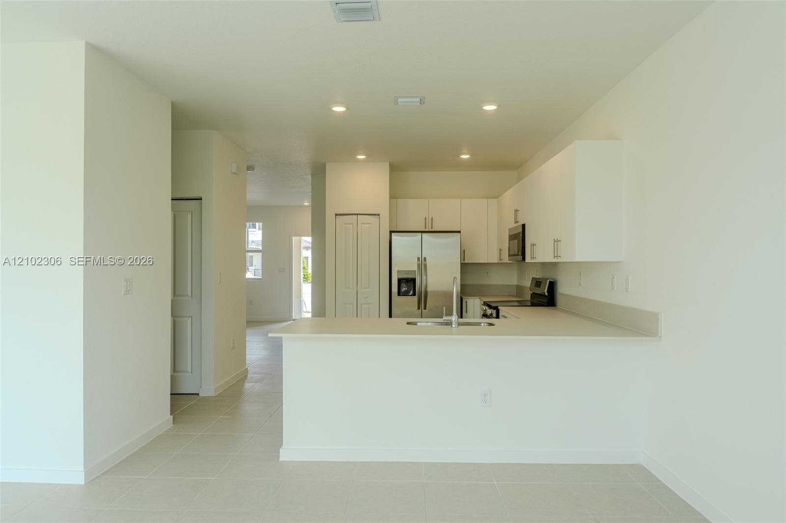 Kitchen featuring white flat-panel cabinetry, a peninsula with a stainless steel sink, tile flooring, recessed lighting, and stainless steel appliances