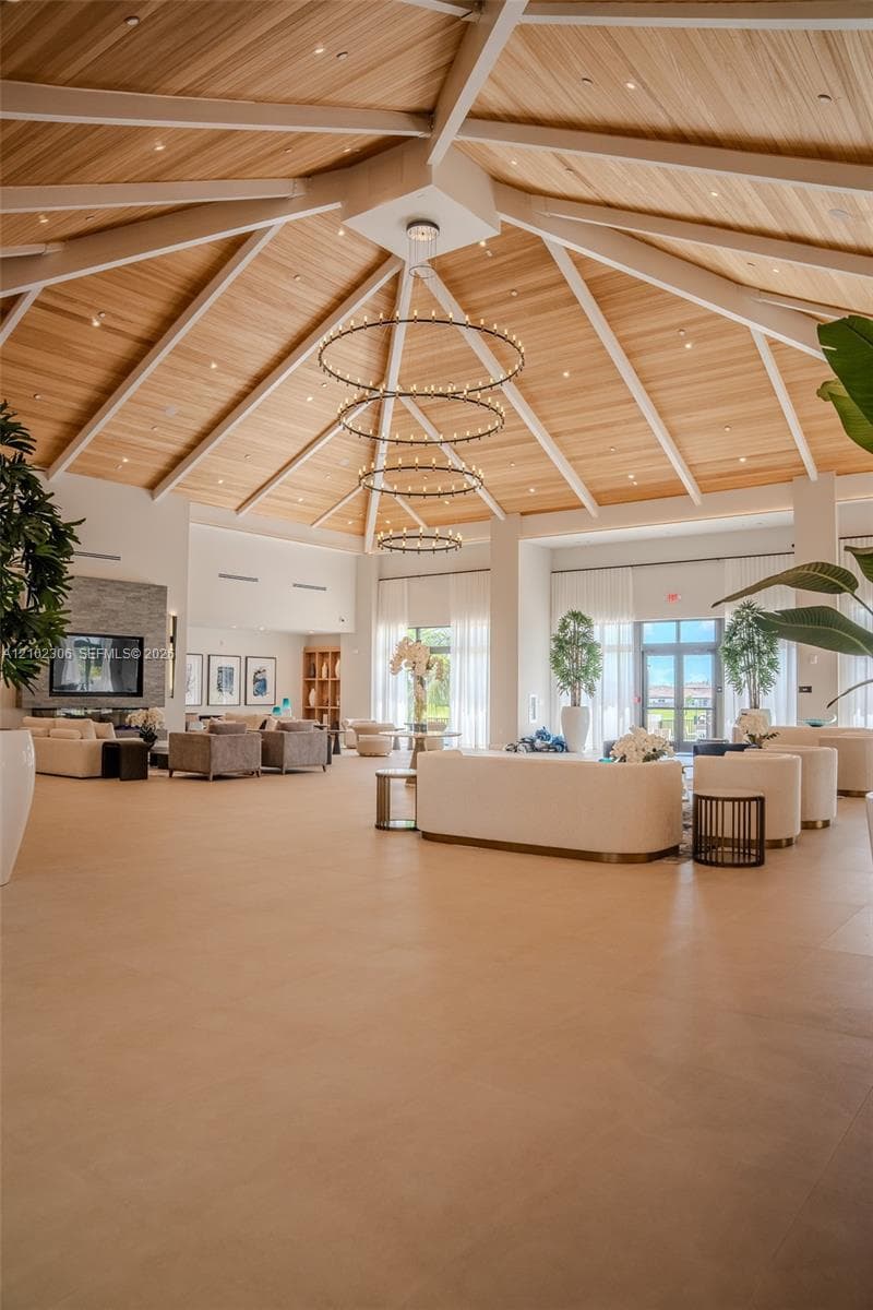 Vaulted wood-plank ceiling with exposed rafters, multi-tiered circular chandelier, large-format tile flooring, stacked-stone fireplace surround, and floor-to-ceiling windows