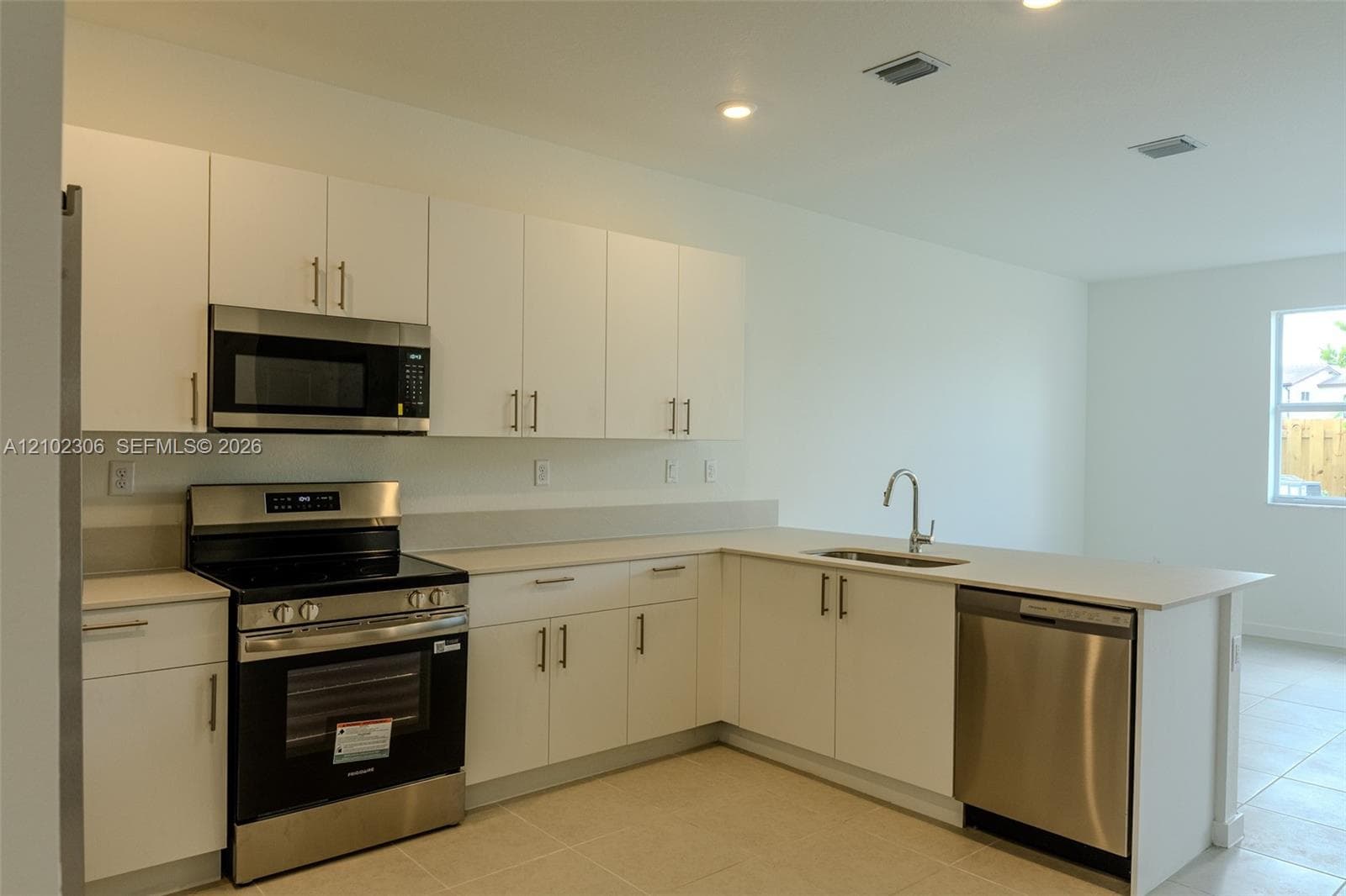 Kitchen featuring white flat-panel cabinetry, light-toned solid surface countertops, stainless steel appliances, and a single-basin undermount sink with a gooseneck faucet