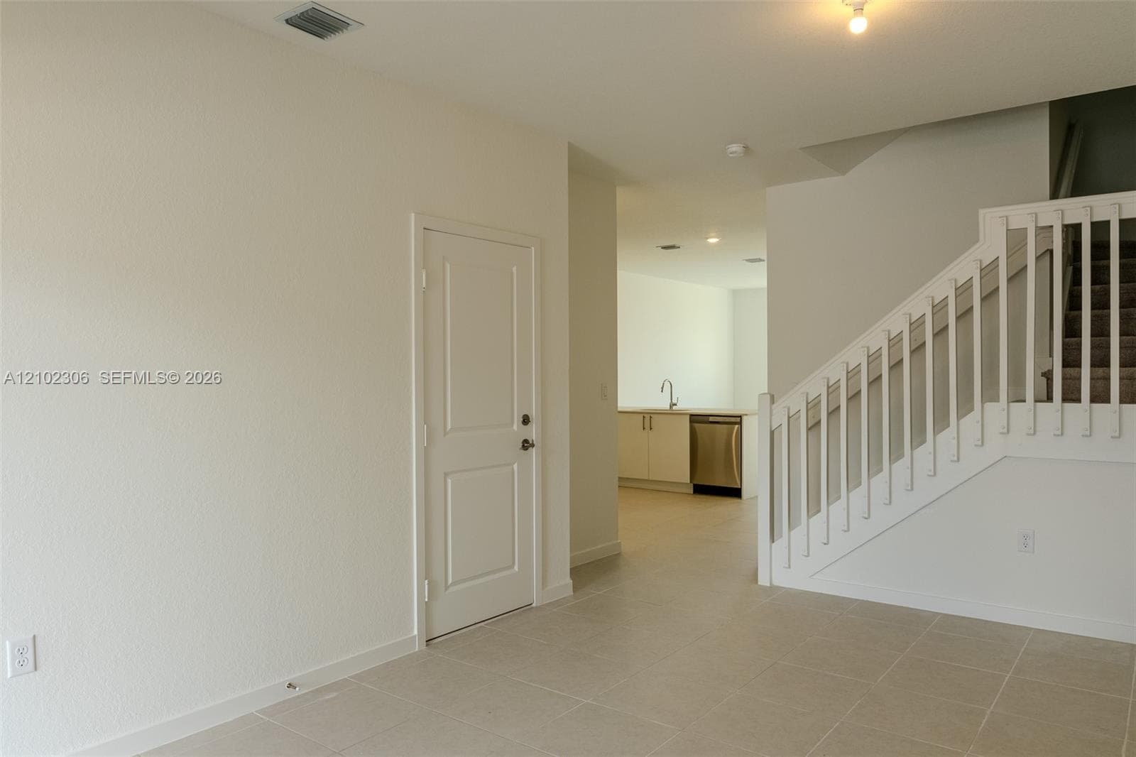 Staircase featuring a white balustrade, neutral tile flooring, and solid-core interior door, with stainless steel kitchen appliances visible in the background