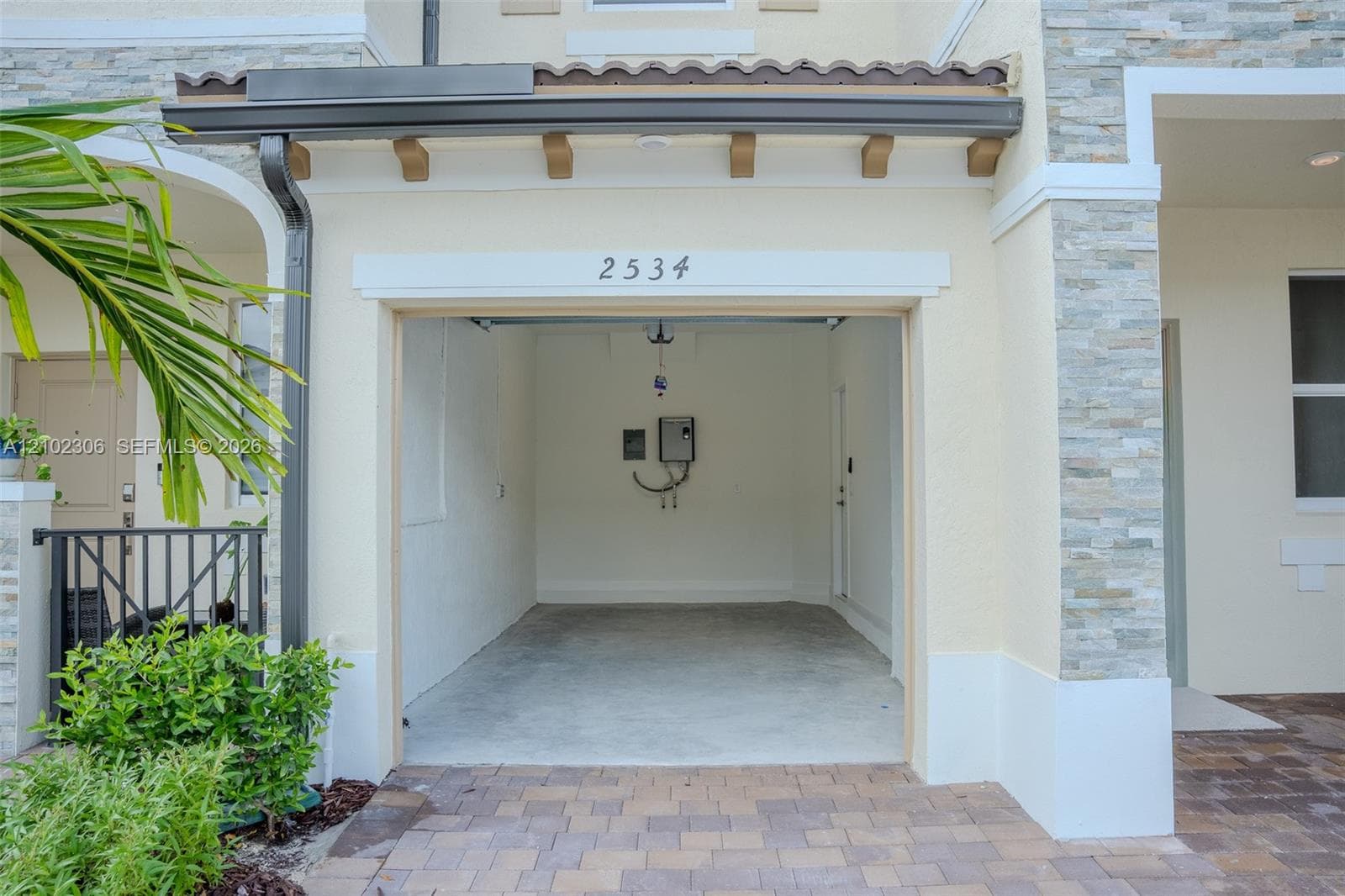 Attached garage featuring stacked stone exterior accents, a concrete floor, and a paver driveway