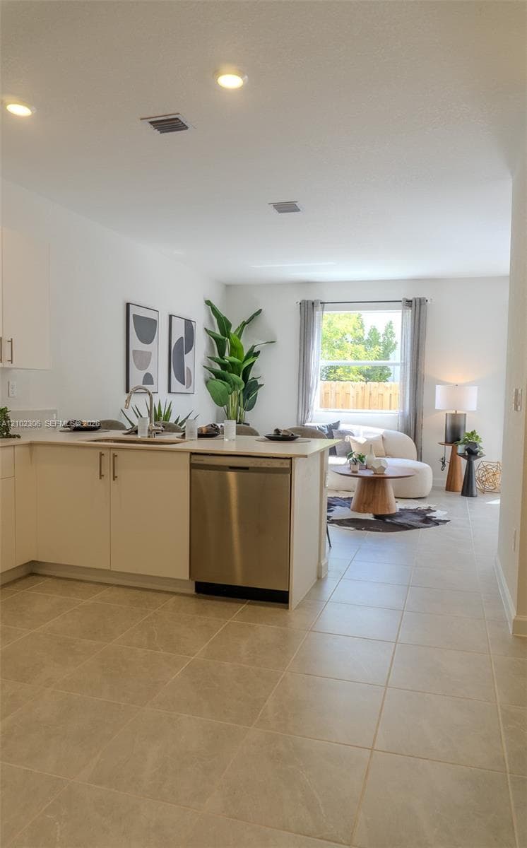 Kitchen featuring a peninsula with solid-surface countertops, stainless steel dishwasher, undermount sink, and neutral tile flooring