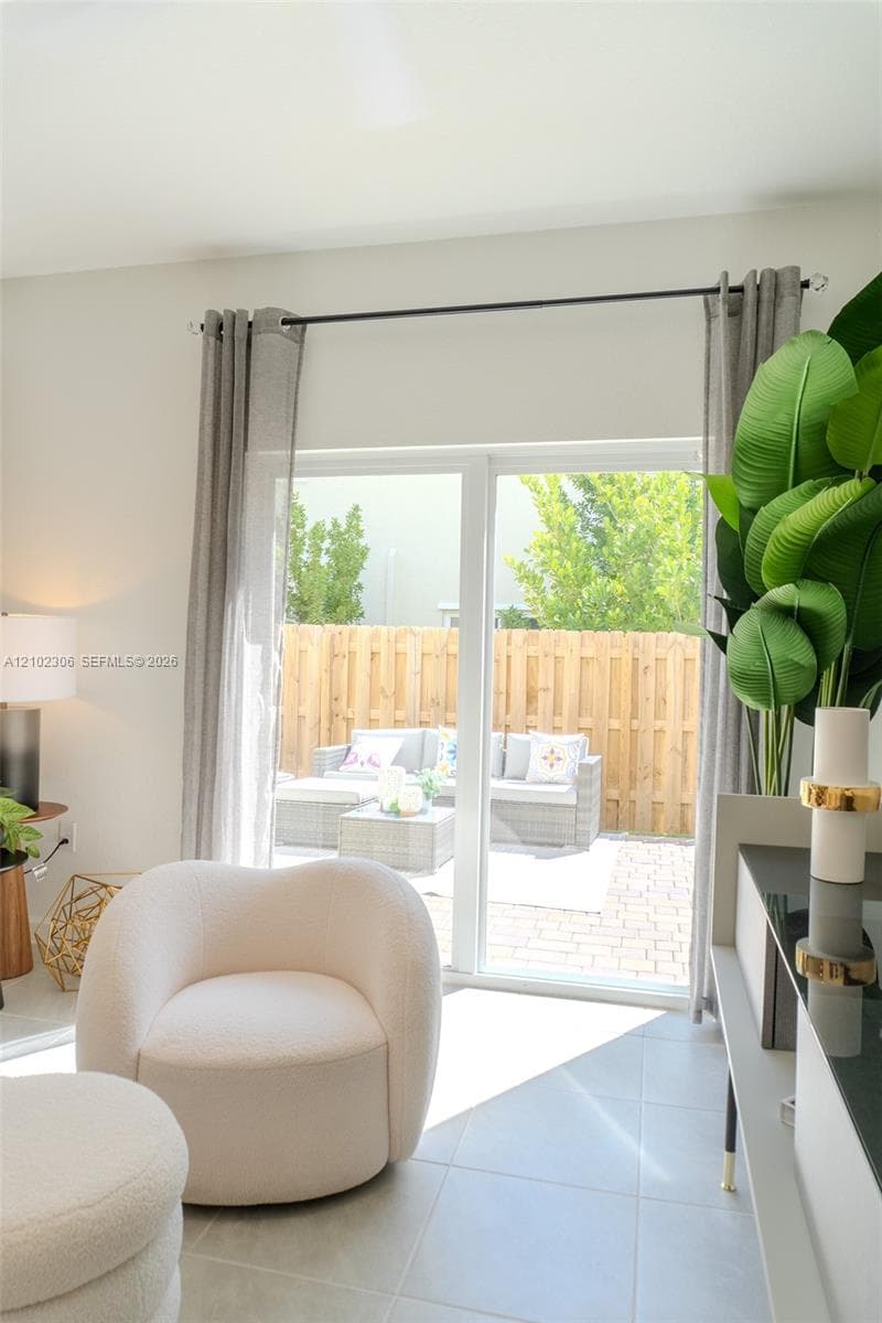 Sliding glass door opening to a paved patio, enclosed by a wood privacy fence, featuring large-format tile flooring