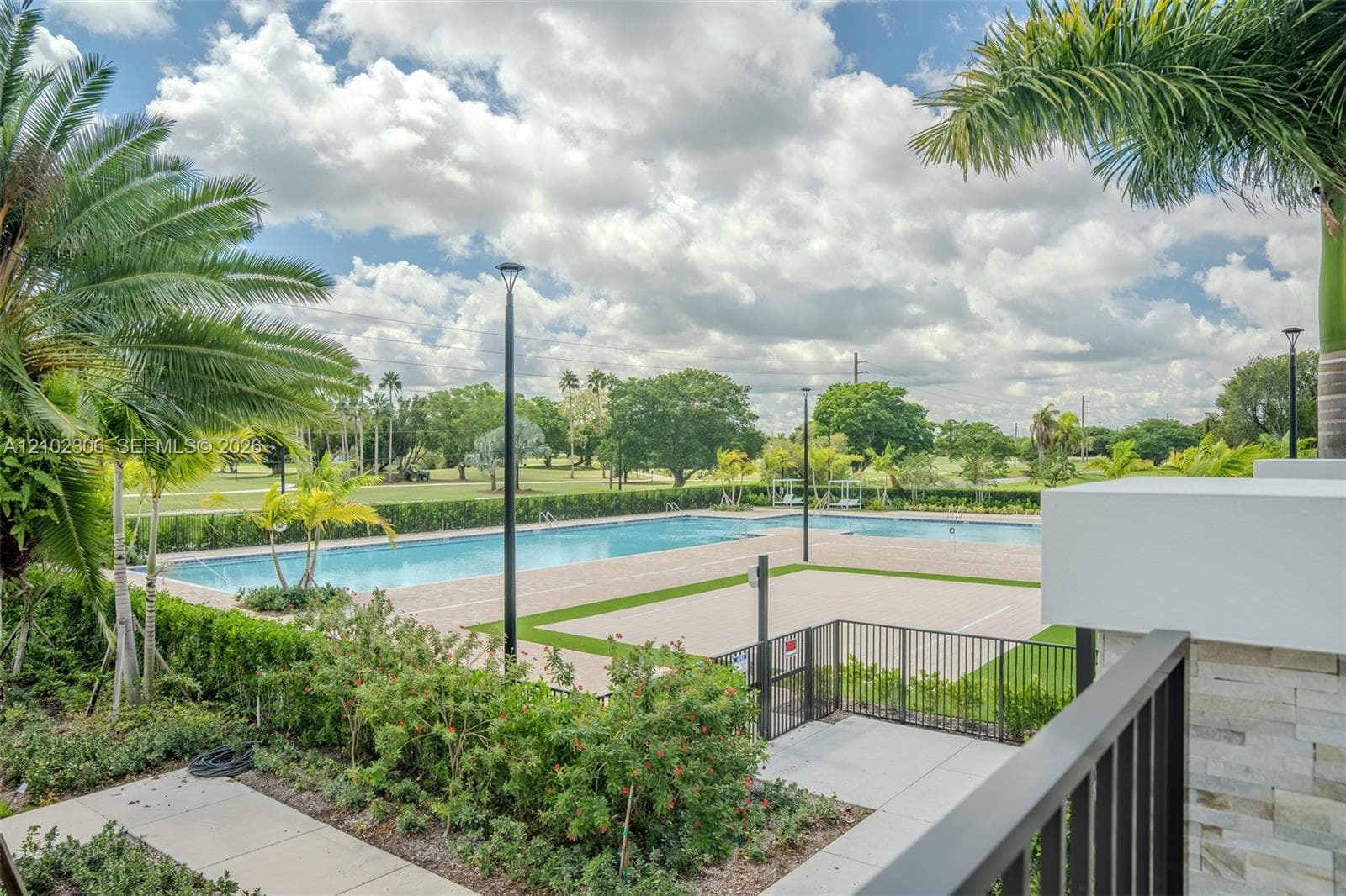 Outdoor recreational area featuring a paved pool deck, swimming pool, pickleball court, and perimeter landscaping