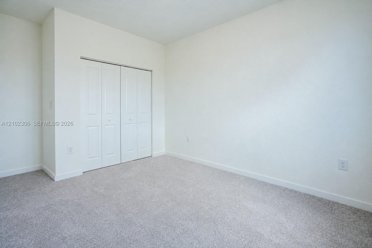 Neutral-toned carpeted flooring, white interior walls, and bi-fold closet doors with raised-panel detailing