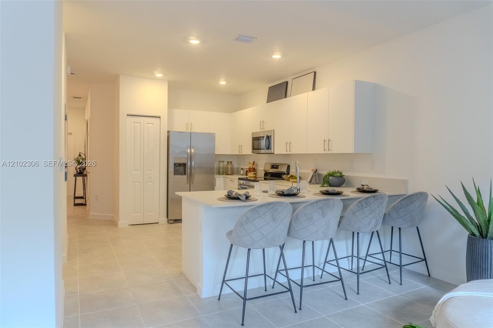 Kitchen featuring white flat-panel cabinetry, a stainless steel refrigerator, built-in microwave, stone-surface breakfast bar, and tile flooring