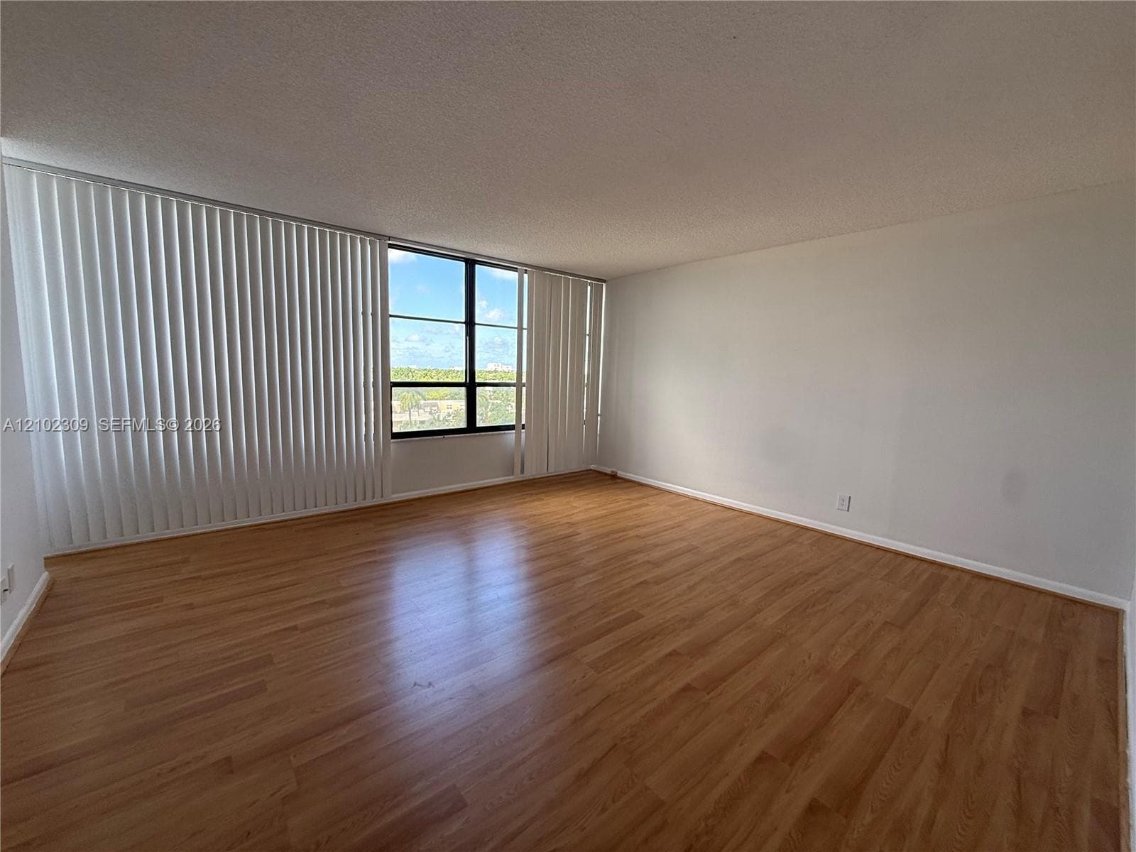 Spacious interior featuring wood-finish flooring, neutral wall tones, and large windows with vertical blinds