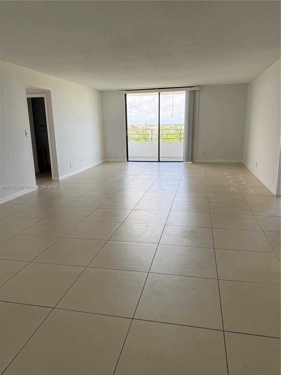 Open-concept living space featuring large-format neutral floor tile and floor-to-ceiling sliding glass doors leading to a private balcony