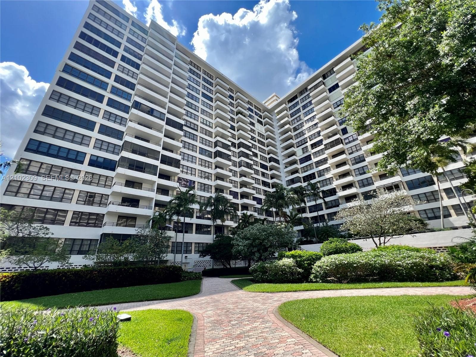 Multi-story high-rise exterior featuring private balconies, masonry facade, and extensive hardscaping with paver walkways and landscaped grounds