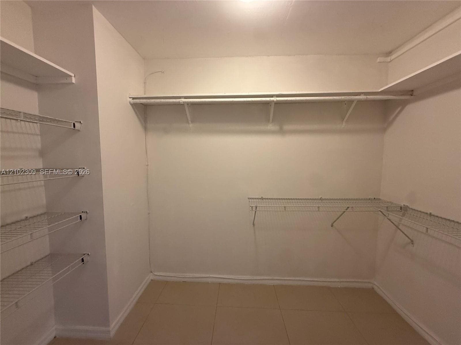 Walk-in storage space featuring ceramic tile flooring, tiered wire shelving units, and extended horizontal rods