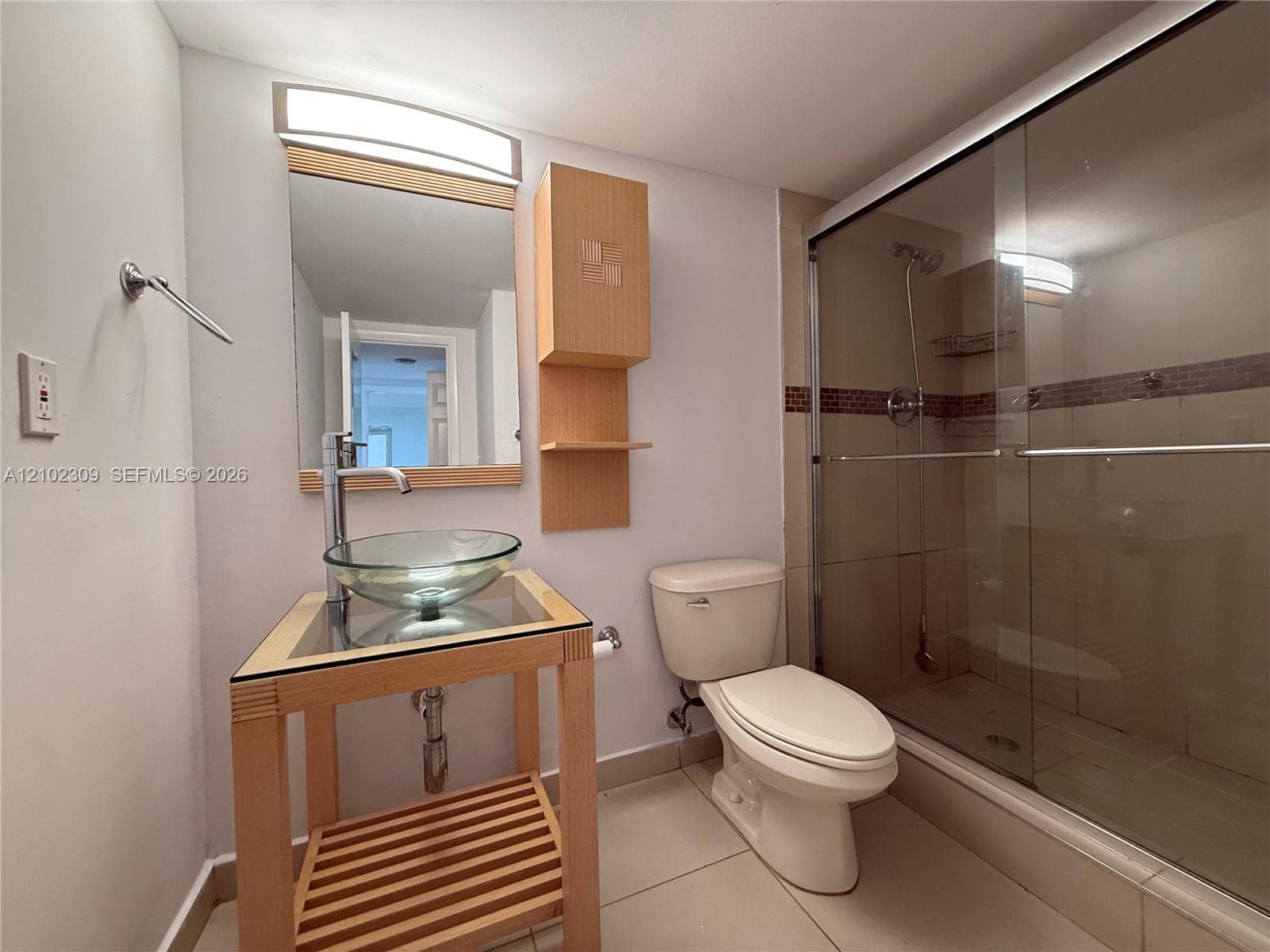 Open-frame wood vanity featuring a glass vessel sink, glass shower enclosure with tile surround, and wall-mounted light fixture
