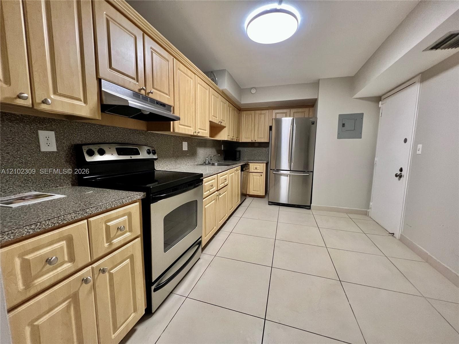 Kitchen featuring wood cabinetry, stone-texture countertops, stainless steel appliances, and large-format tile flooring